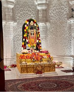 the statue is decorated with flowers and other things in front of an ornate white wall