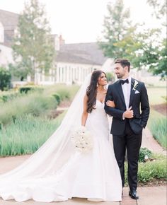 a bride and groom walking together in front of a house