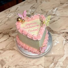 a heart shaped cake with pink frosting and butterflies on top sitting on a marble table