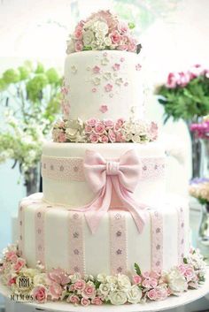 a three tiered cake with pink flowers and bows on the top is sitting on a table