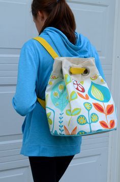 a woman wearing a blue hoodie carrying a white and yellow bag with flowers on it