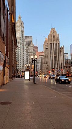 an empty city street with tall buildings in the back ground and cars driving down it