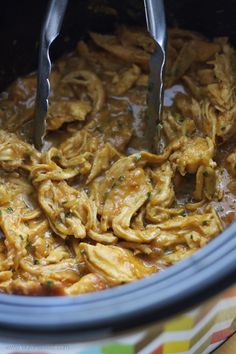 two tongs in a slow cooker full of pasta and meat sauce with parsley on top