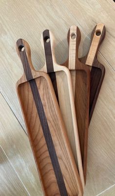 three wooden cutting boards sitting on top of a table next to each other with handles