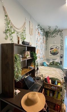 a room with a bed, desk and shelves filled with plants on the wall next to it