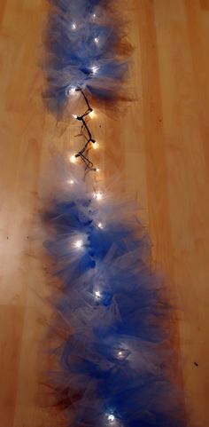 a blue christmas tree with white lights on it's branches is shown in front of a wooden floor