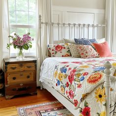 a white bed topped with lots of pillows next to a wooden dresser and window sill