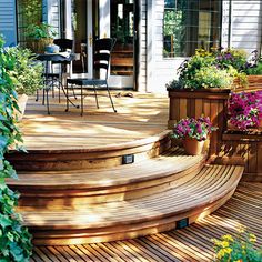 a wooden deck with potted plants and flowers on the steps leading to an outdoor dining area