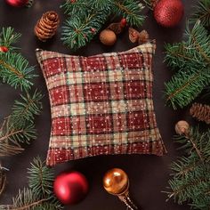 a red plaid pillow sitting on top of a table next to christmas ornaments and pine cones