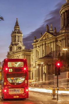 a red double decker bus driving down a street in front of tall buildings at night