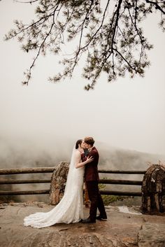 a bride and groom kissing on top of a mountain in front of a foggy sky