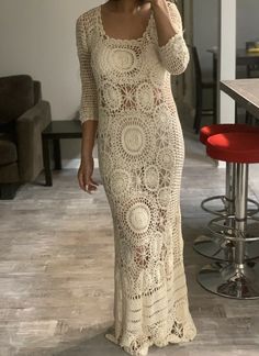 a woman in a white crochet dress talking on a cell phone while standing next to a bar