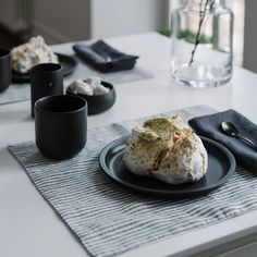 a black plate topped with food on top of a table next to cups and saucers