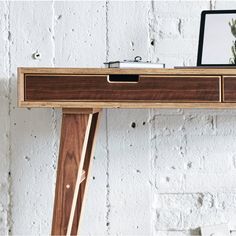 a laptop computer sitting on top of a wooden desk next to a white brick wall