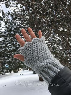 a hand that is wearing a knitted glove in front of some snow covered trees