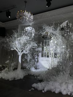 snow covered trees in front of a window and chandelier