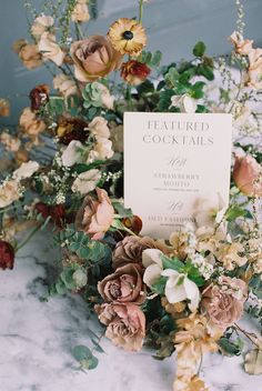 an arrangement of flowers and greenery on a marble countertop with a sign that reads, featured cocktails