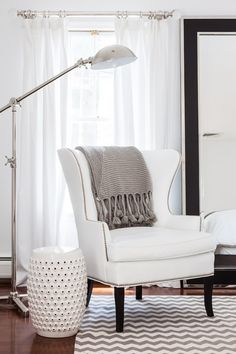 a white chair sitting in front of a window next to a lamp and a rug