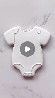 a white baby bodysuit with a video play button on it's left chest