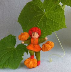 a small doll is standing next to a large green leaf and holding something in her hands