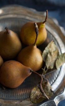 four pears in a silver bowl with leaves on the side and a knife next to them