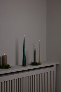 three candles sitting on top of a white shelf next to a radiator in a room