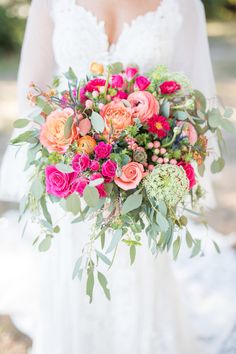 a woman holding a bouquet of flowers in her hands and wearing a wedding dress with lace sleeves