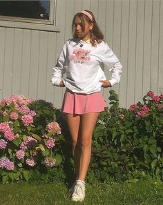 a girl is standing in the grass with her hands on her hips wearing a white sweatshirt and pink skirt