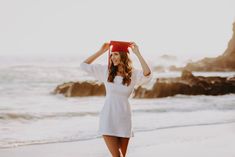 a woman with a red hat on her head walking along the beach in front of the ocean