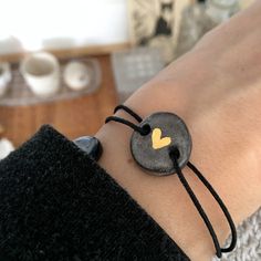 a person wearing a black bracelet with a yellow heart on it's side and a string attached to the wrist