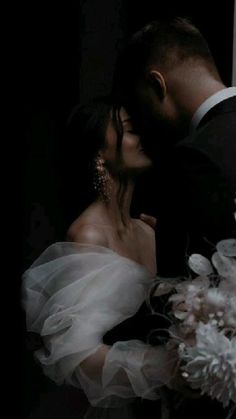 a bride and groom kissing in front of a window with white flowers on the bouquet