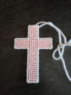 a pink cross on a black surface next to a white string and some yarns