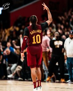 a man in maroon and black uniform standing on top of a basketball court with his hand up