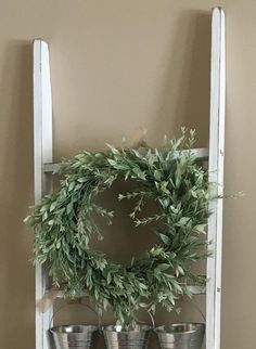 an old ladder is used as a shelf to hold three buckets and a wreath