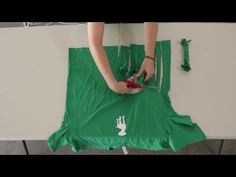 a person cutting fabric with scissors on a table next to a white wall and green cloth