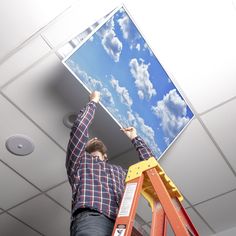 a man standing on a stepladder holding up a large picture in the air