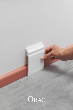 a hand is holding the corner of a white wall with pink trim and an orange strip