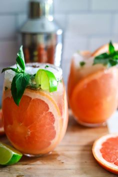 two grapefruit margaritas with lime and mint garnish sit on a cutting board