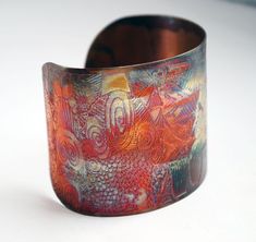 a close up of a metal bracelet on a white surface with an orange and red design