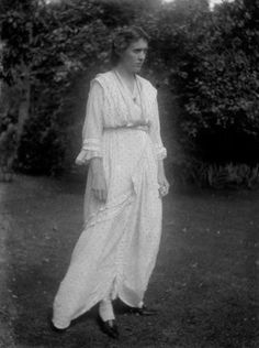 an old black and white photo of a woman in a long dress standing on grass