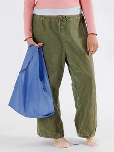 a woman in green pants and pink shirt holding a blue bag with her right hand