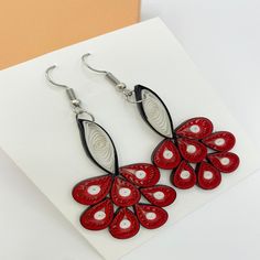 a pair of red and black earrings on top of a white piece of paper next to a card