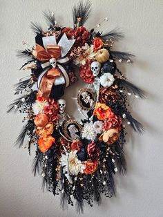 a wreath with feathers, flowers and skulls on the front is hanging on a wall