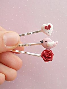 someone is holding two tiny hair pins with hearts and flowers on them in their fingers