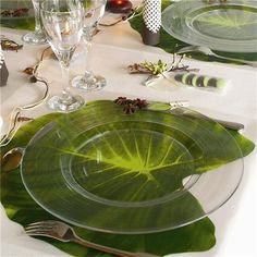 the table is set with plates, silverware and green leaf napkins on it