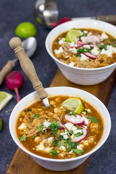 two white bowls filled with soup and garnished with cilantro, radishes, limes