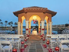 an outdoor wedding venue with white chairs and red flowers on the aisle, lit up by candles