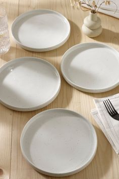 four white plates on a wooden table with forks and napkins next to each other