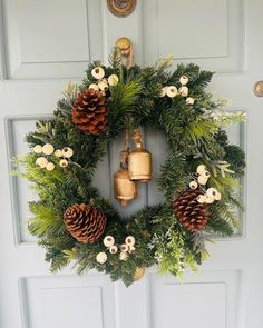 a wreath with pine cones and bells hanging on the front door, decorated with greenery