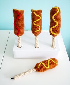 three crocheted hot dogs with mustard and ketchup on them sitting on a white surface